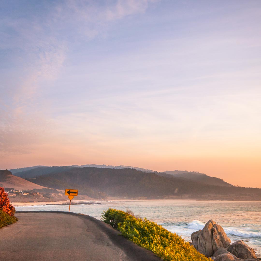 Carmel's scenic road curves to the left as the sun sets over the ocean.