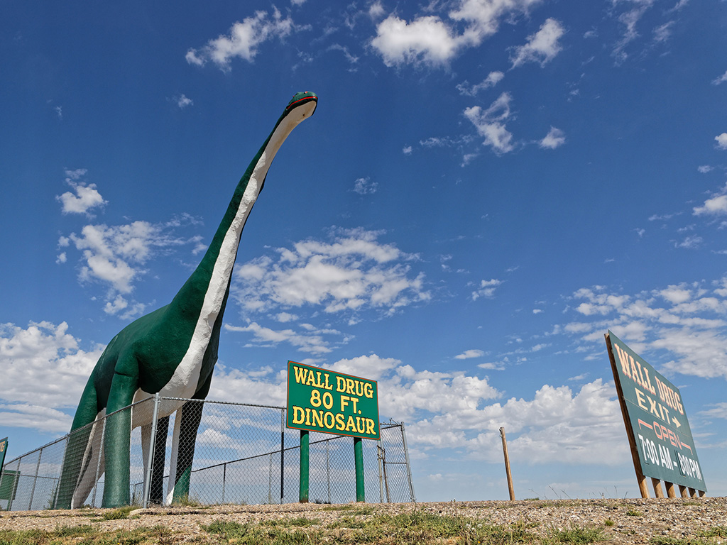 green dinosaur statue with blue sky and a sign that says Wall Drug